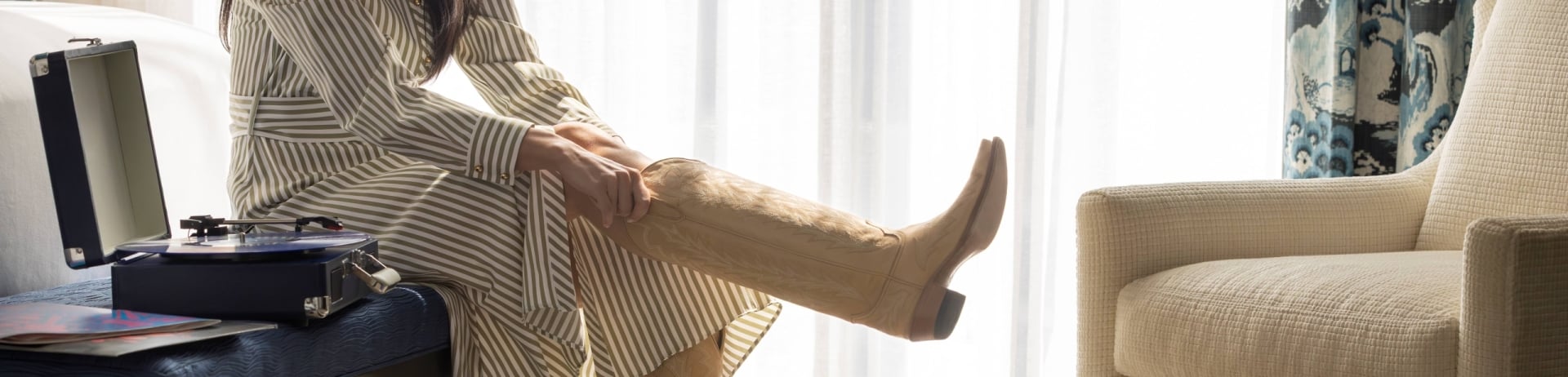 woman putting on cowboy boots in hotel room